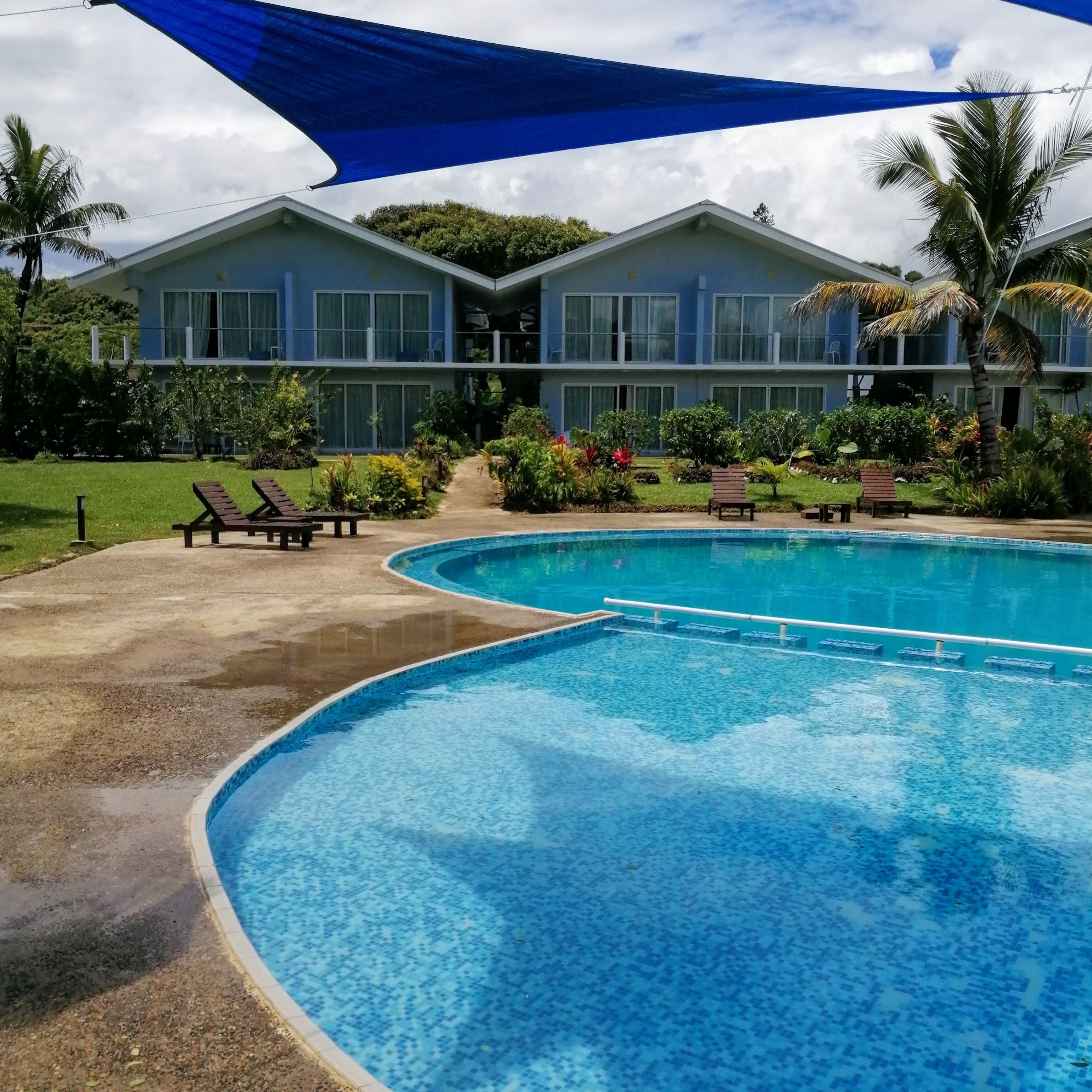 Una piscina con sillas de descanso y un edificio con varios balcones al fondo.