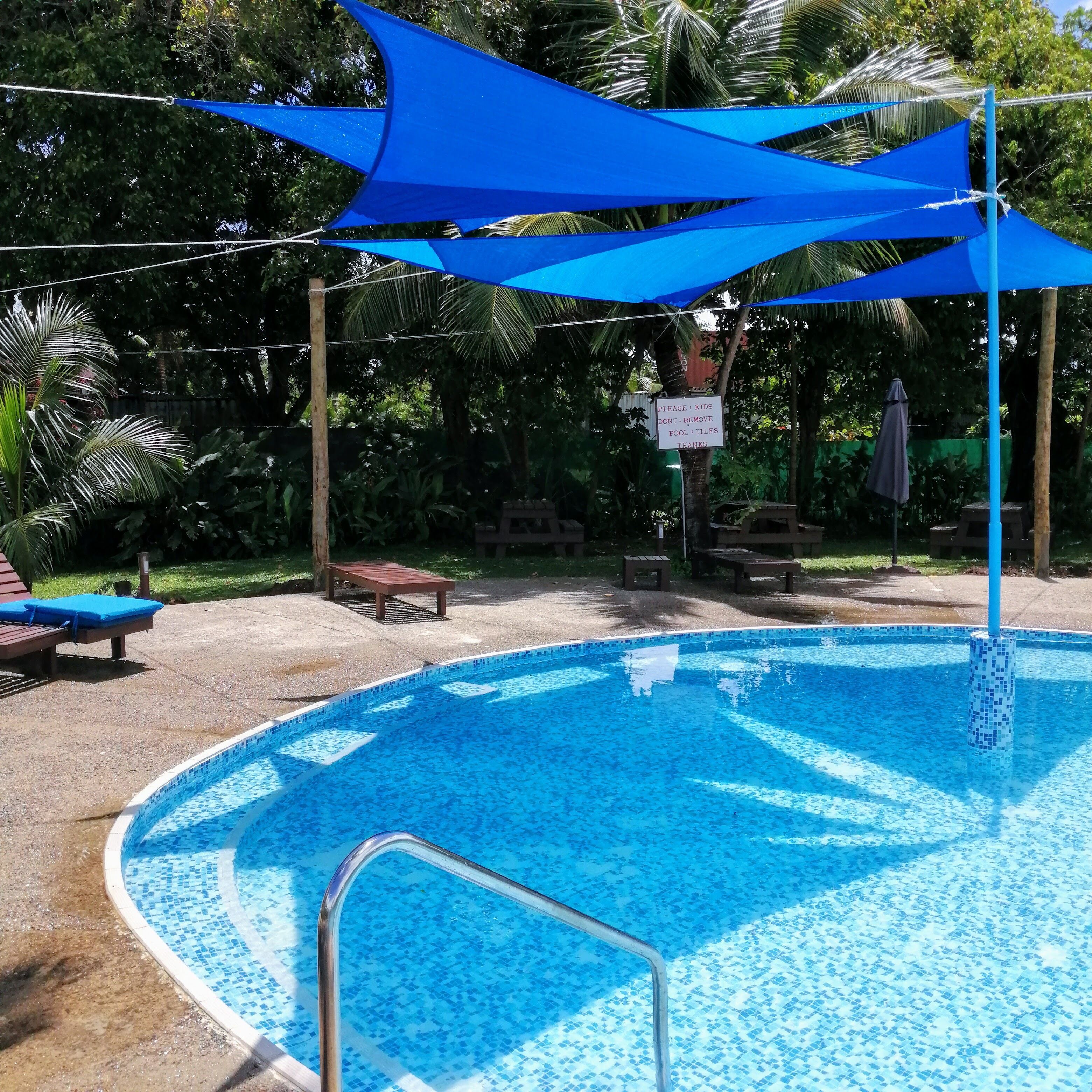 A swimming pool with a tiled edge, surrounded by lounge chairs and a shaded area with a sign.