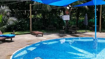 A swimming pool with a tiled edge, surrounded by lounge chairs and a shaded area with a sign.