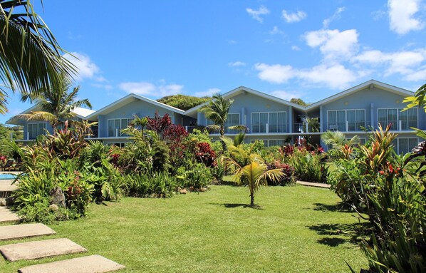 Un edificio de dos pisos con césped cuidado y plantas tropicales.