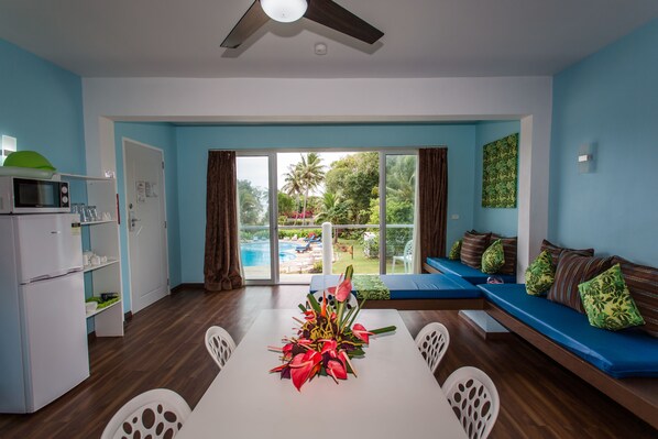 A modern living room with a dining area, a ceiling fan, a view of a pool, and a sofa with cushions.