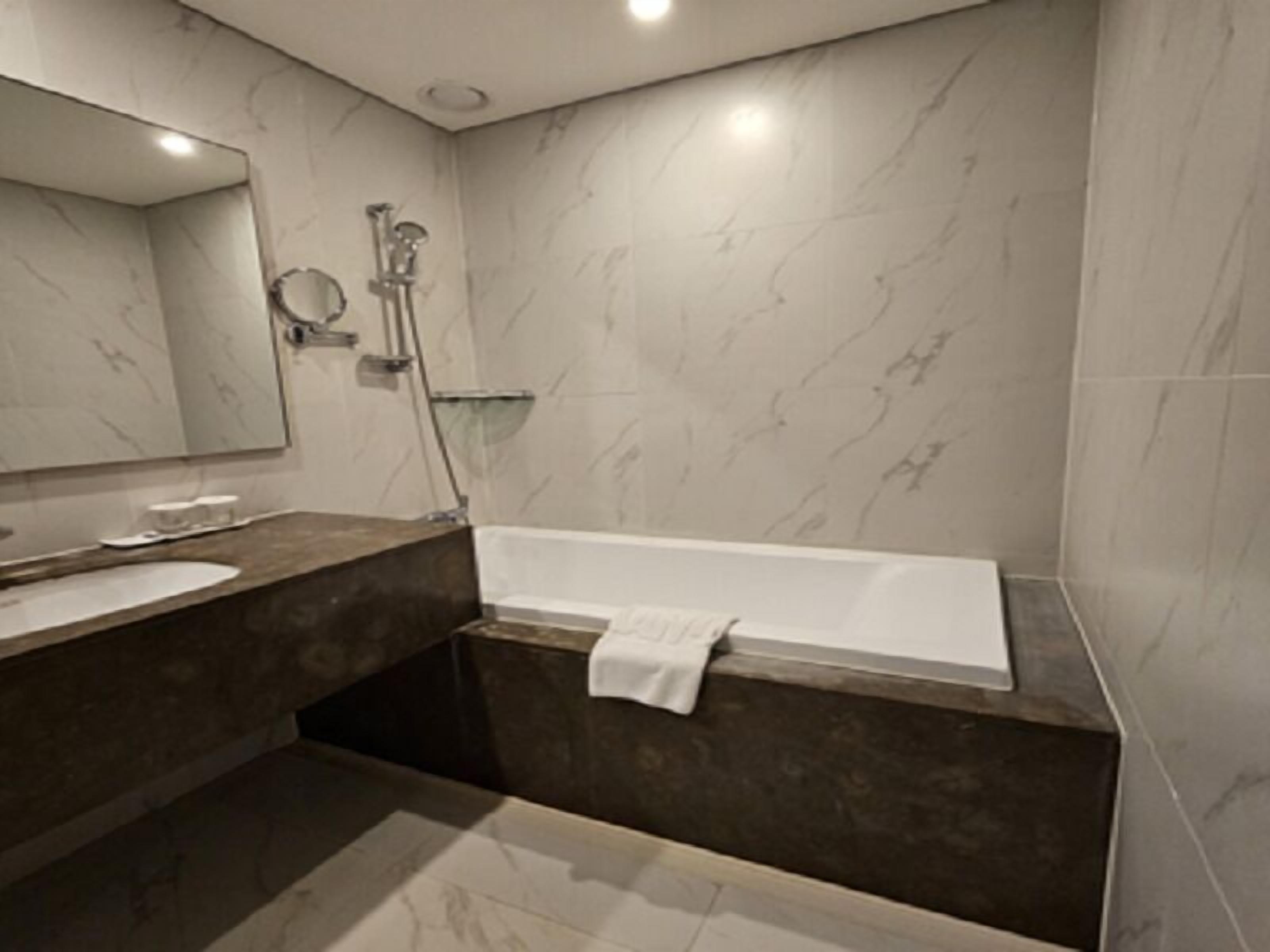 A modern bathroom with a marble vanity, a large mirror, a bathtub, and a shower area.