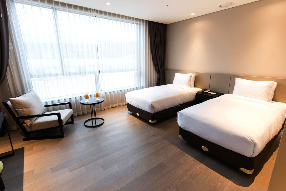 A hotel room with two beds, a sofa, a small round table, and a view of the city through large windows.