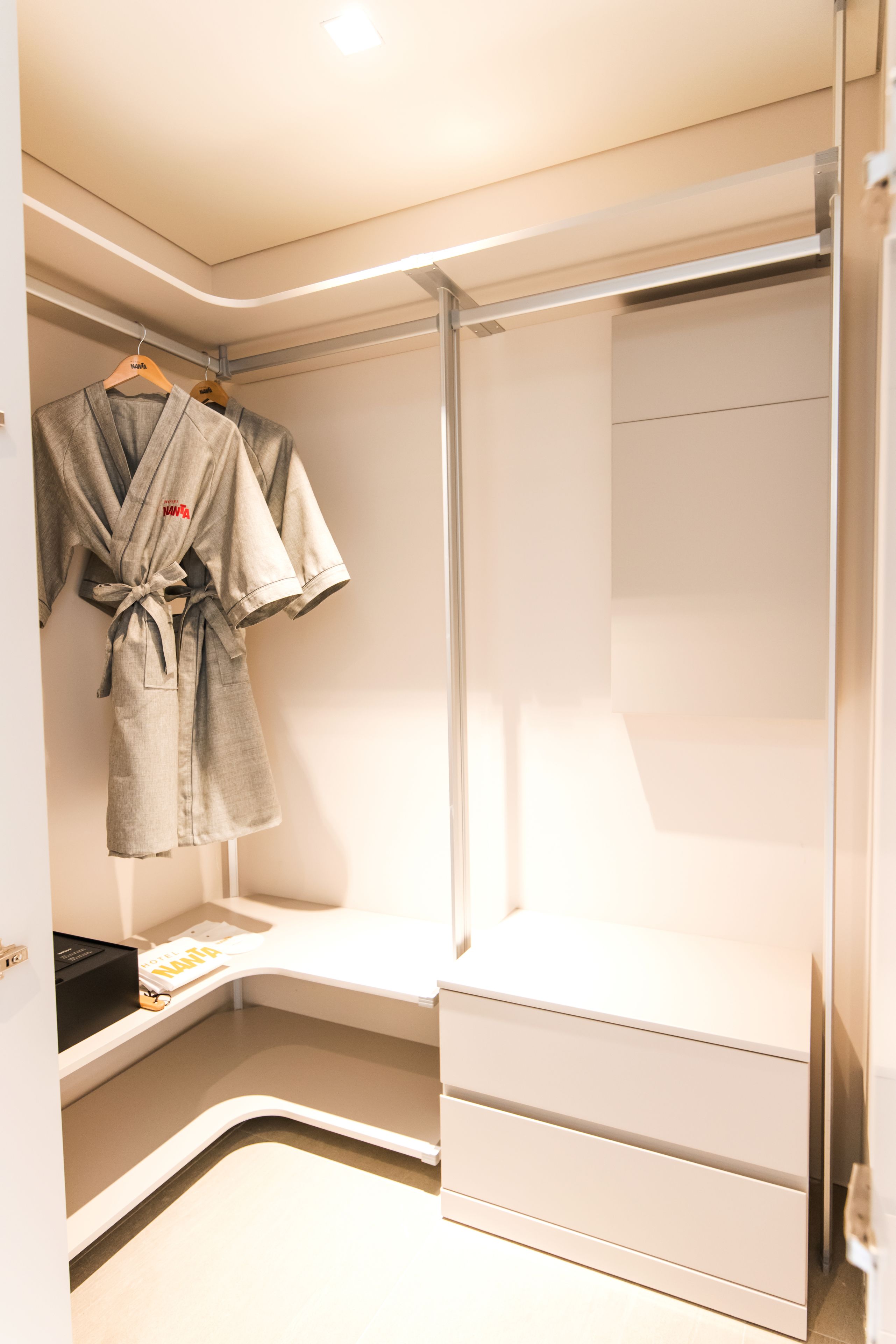 Un baño moderno con cabina de ducha de vidrio, una bata colgada en un perchero y una encimera blanca con una revista.