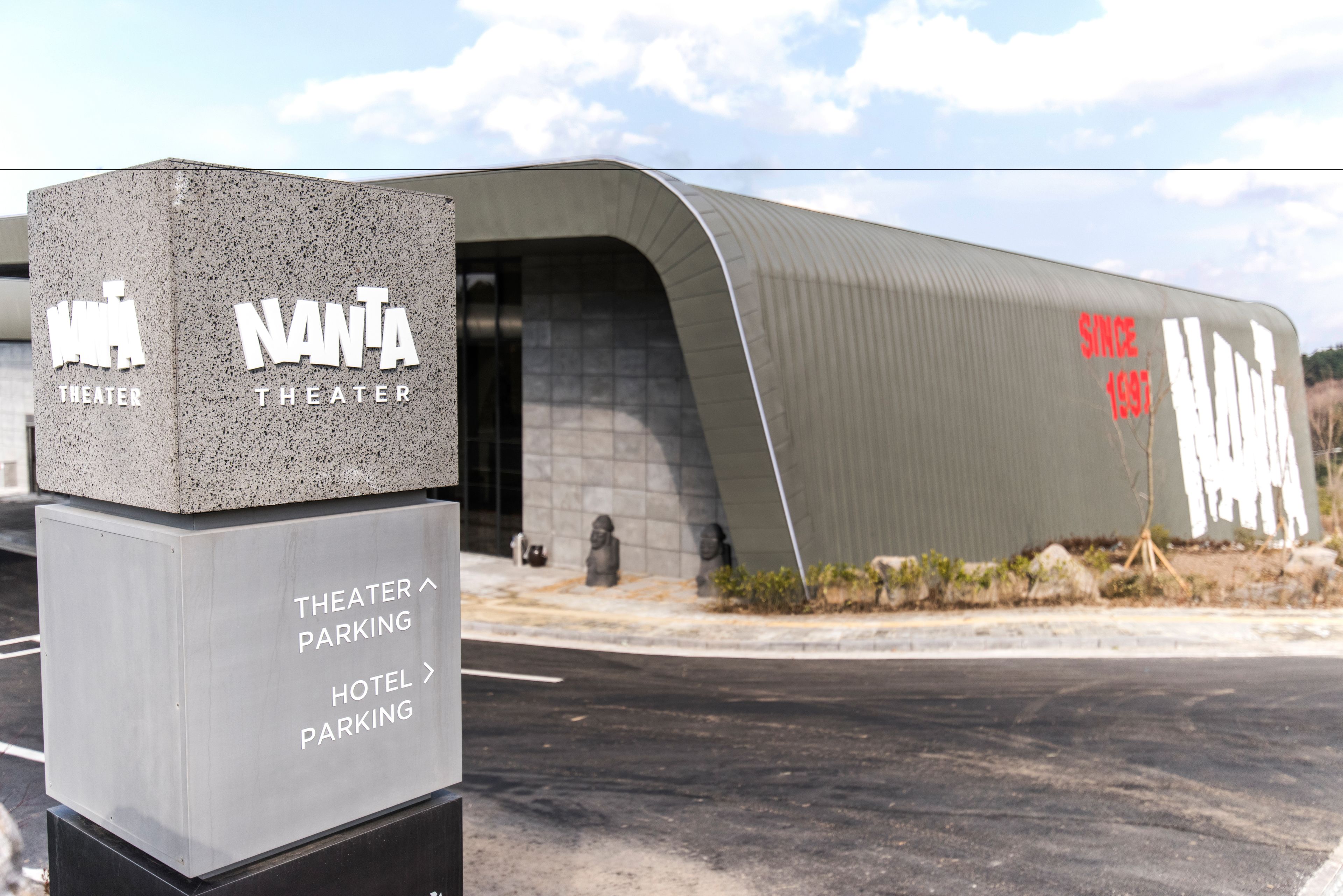 Un edificio moderno con un cartel que indica las direcciones hacia 'NANTA THEATER' y 'THEATER PARKING'.