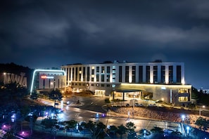 Un hotel moderno con un llamativo letrero de 'NAVA THEATER', un amplio estacionamiento y una entrada bien iluminada.