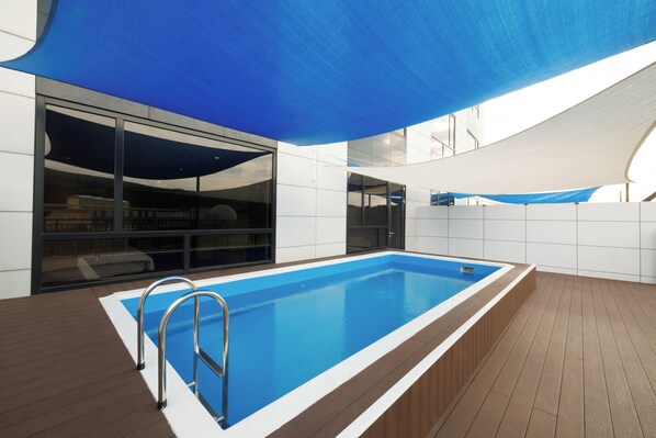 Una piscina interior moderna con agua azul cristalina, rodeada de una terraza de madera y paredes de baldosas blancas.