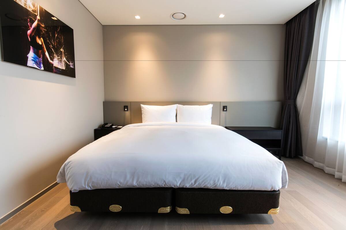 A modern hotel room with a large bed, a bedside table, and a wall-mounted TV.
