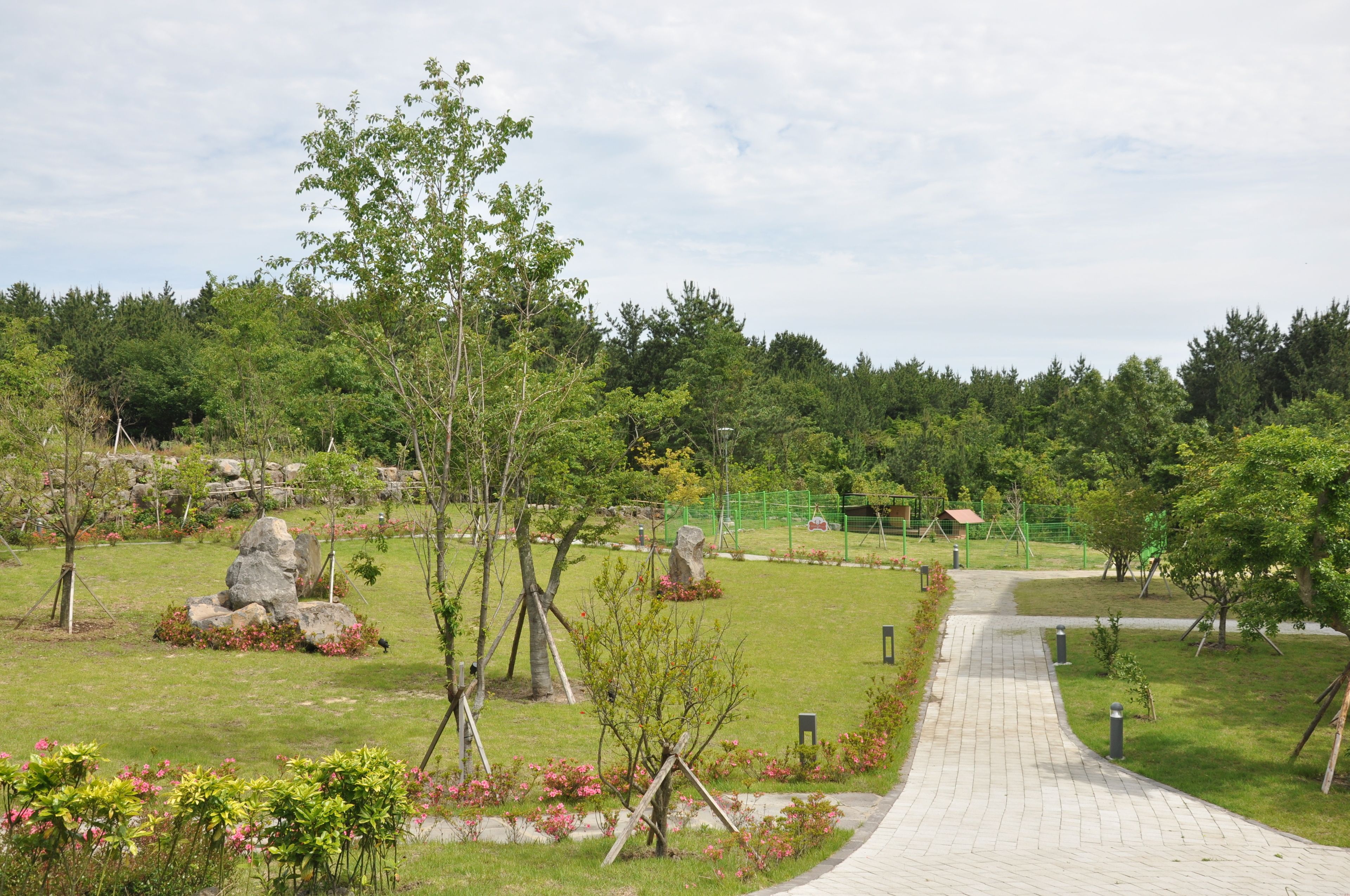 A paved pathway leading through a park with trees, rocks, and a playground.