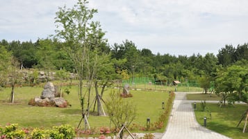 A paved pathway leading through a park with trees, rocks, and a playground.