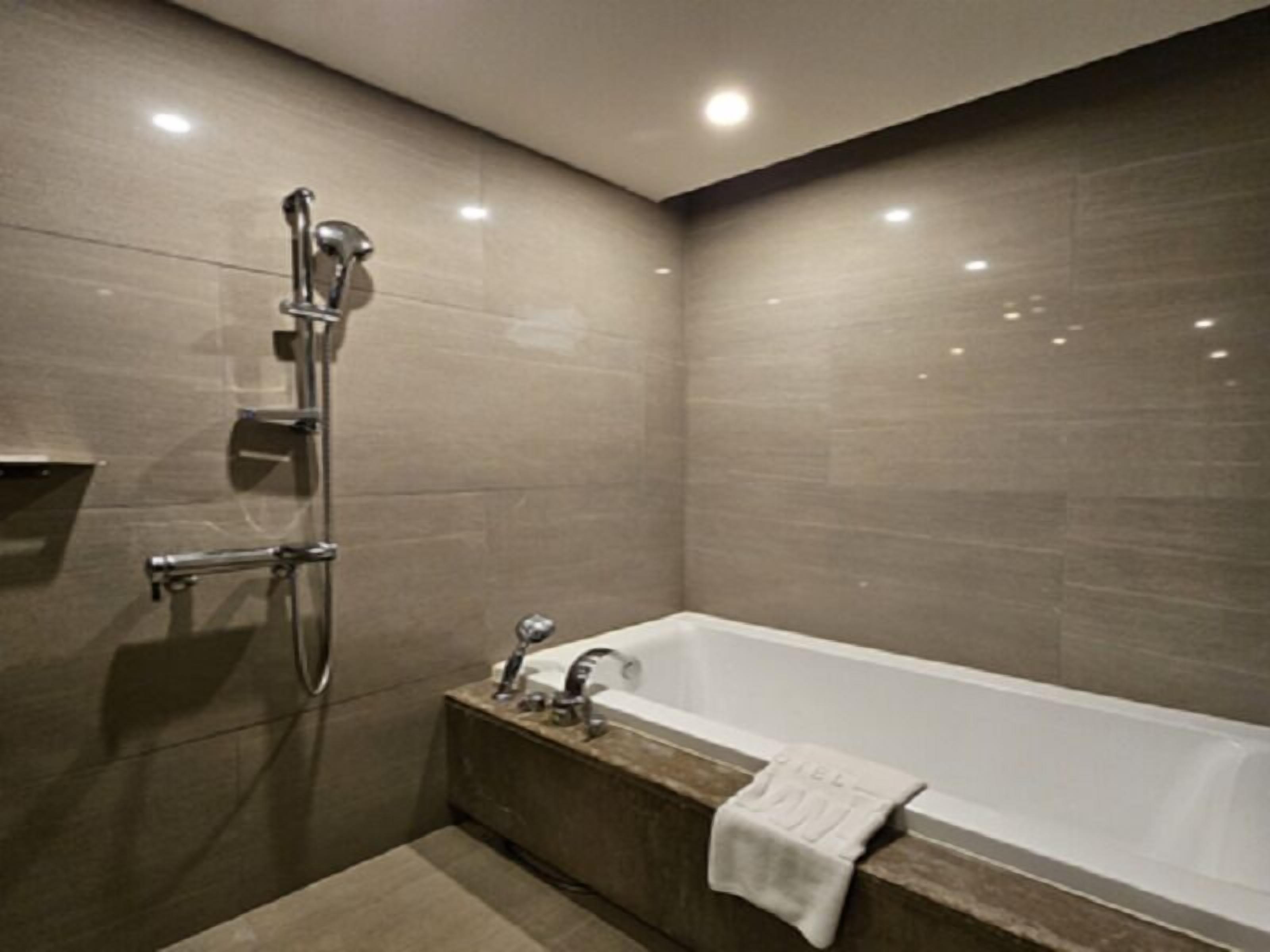A modern bathroom with a bathtub, shower, and a towel on the edge.