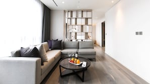A modern living room with a grey sofa, a round coffee table with fruits and wine glasses, and a built-in bookshelf. - Hotel Nanta Jeju (Jeju City)