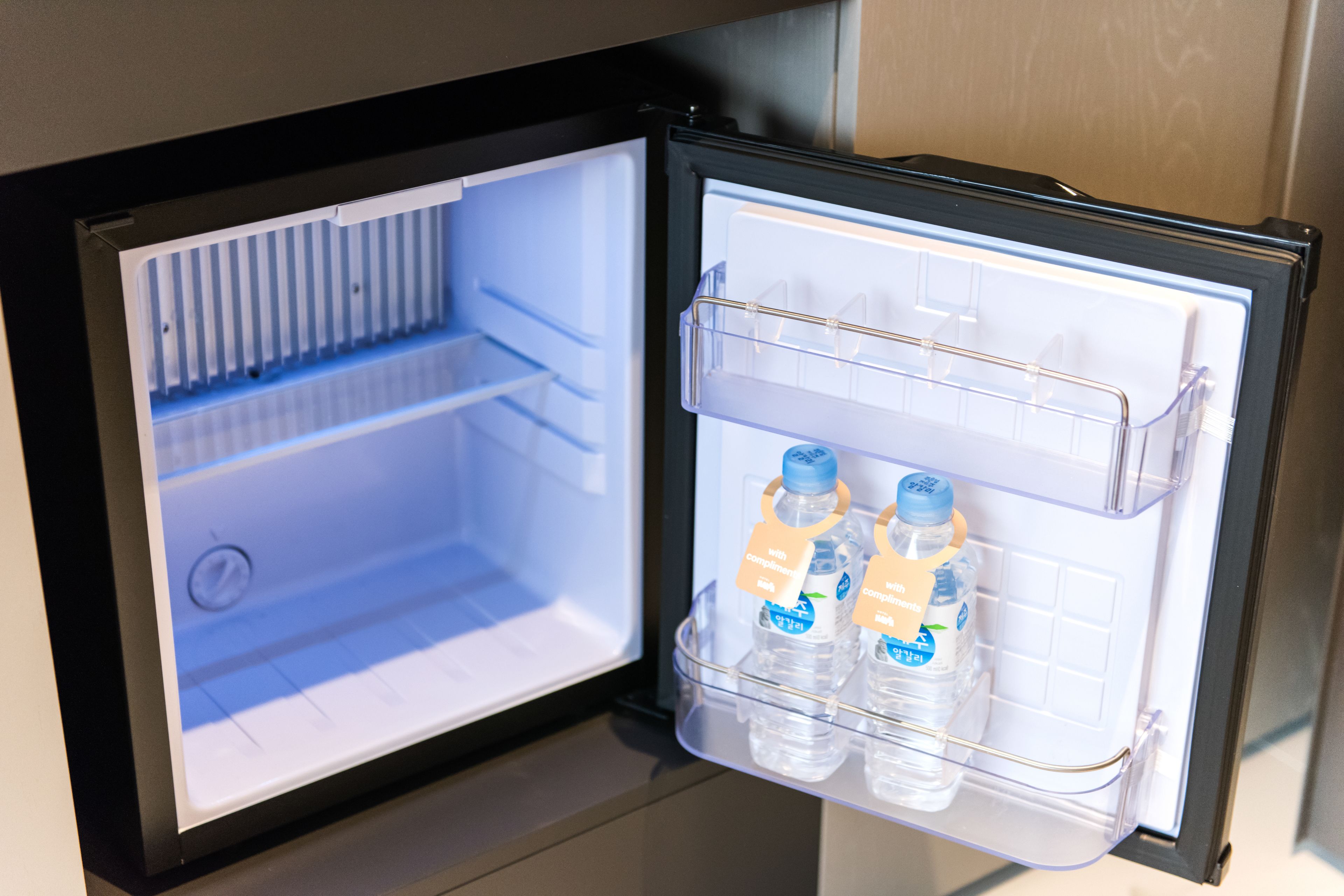 An open refrigerator with two water bottles and a clear plastic shelf.