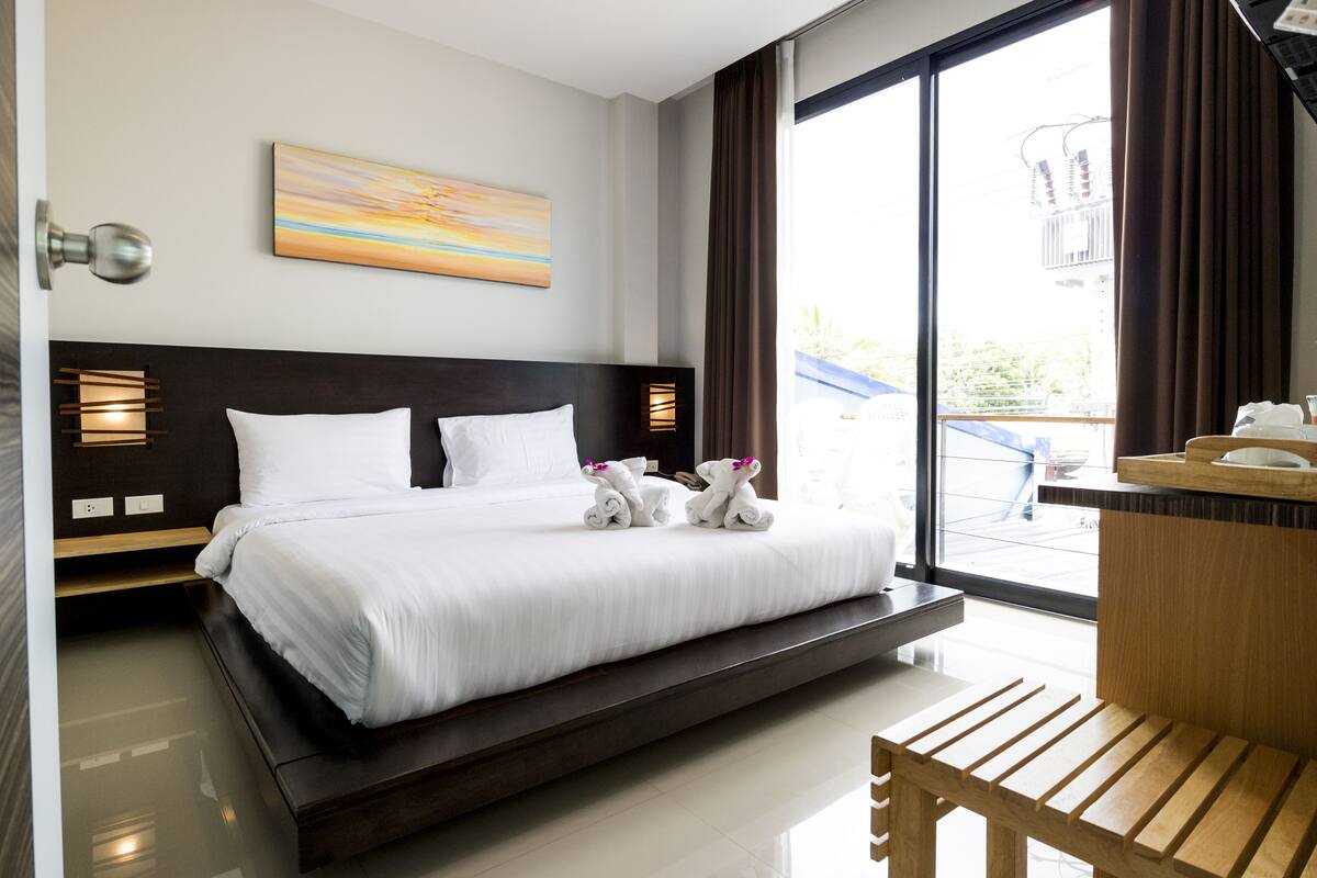 Habitación de hotel con una cama grande, un banco de madera, un escritorio y vistas al exterior.