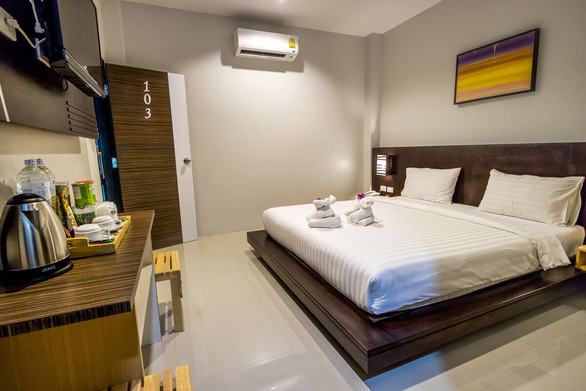 Una habitación de hotel con cama, mesita de noche y aire acondicionado instalado en la pared.