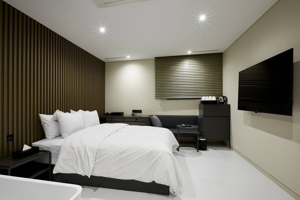 A modern bedroom with a large bed, bedside tables, a desk, and a TV mounted on the wall.