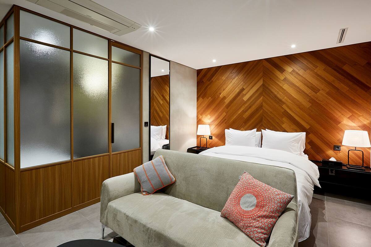 A hotel room with a bed, a sofa, a wardrobe, and a nightstand with lamps.