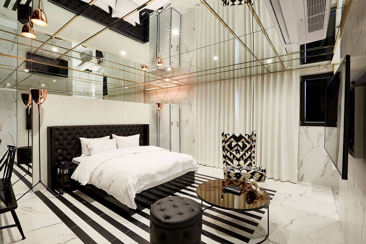 A modern bedroom with a large bed, a glass partition, a round coffee table, and a patterned rug.