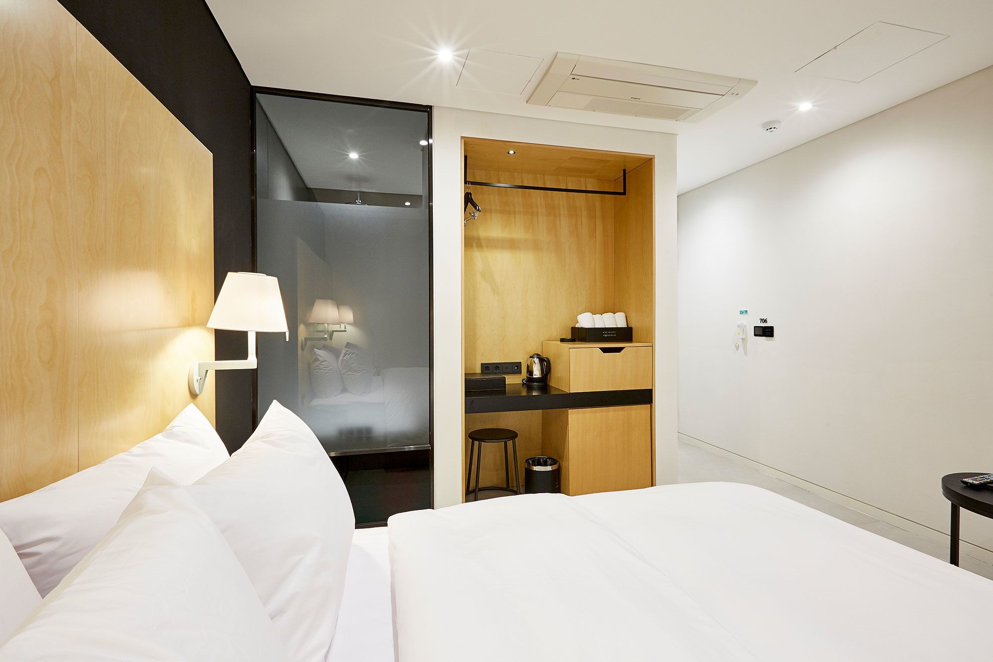 A modern hotel room with a large bed, a small desk, a shower area, and a wooden cabinet with toiletries.