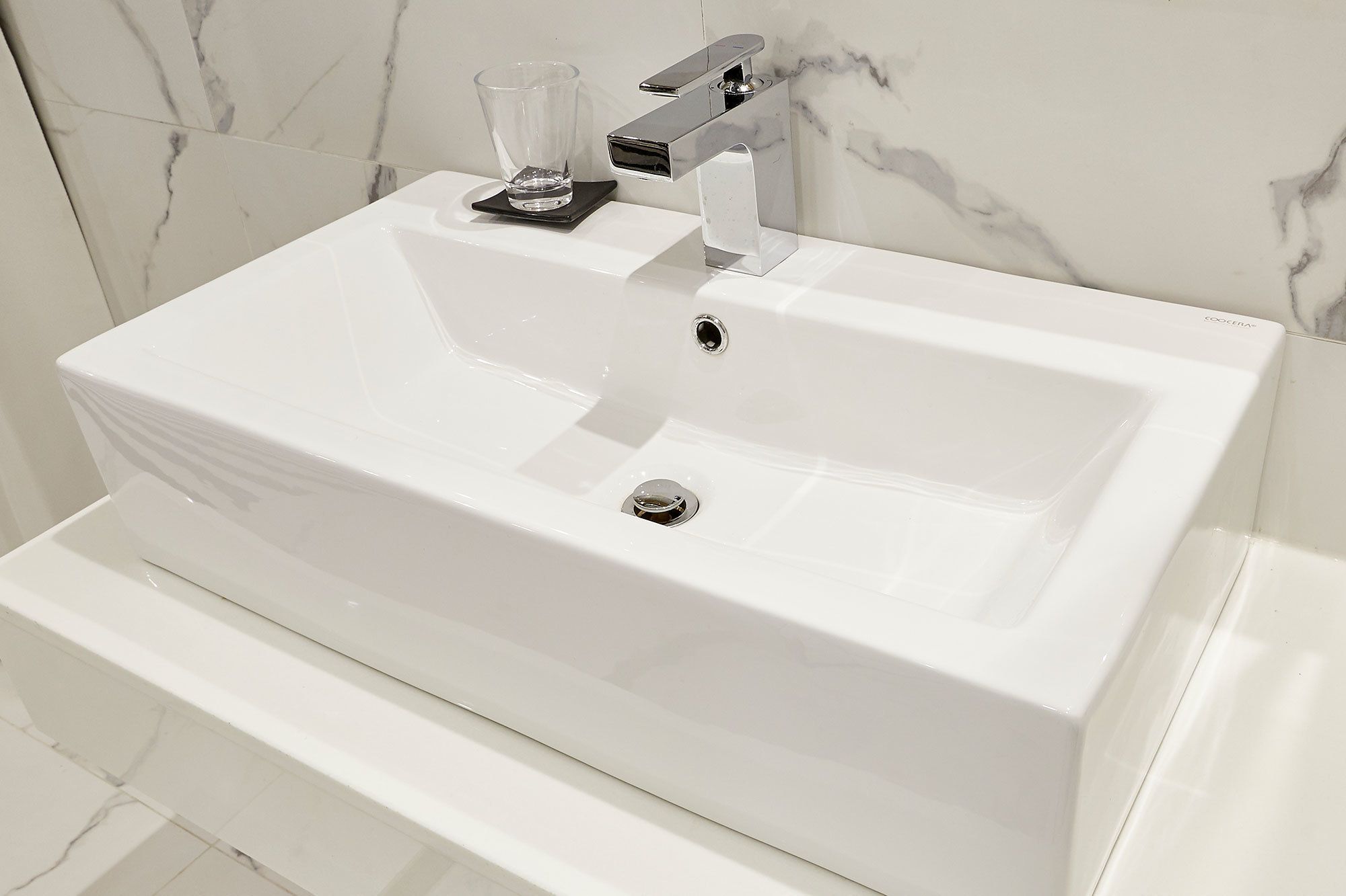 Un lavabo bianco con un rubinetto moderno e un bicchiere sul ripiano.