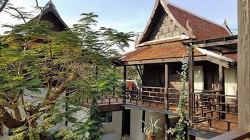 Uma casa de madeira tradicional com telhado de telhas, varanda e área de jardim com árvores.