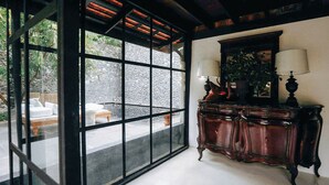 Quarto com uma grande porta de vidro que dá para uma área externa, um armário de madeira com duas luminárias e uma parede de pedra visível através da porta.