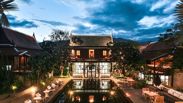 Um edifício tradicional com uma piscina no centro, rodeado por área externa com mesas e cadeiras e plantas em vasos.