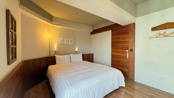 Un dormitorio con cabecera de madera, una cama grande con ropa de cama blanca, una lámpara fijada a la pared y una puerta de madera.