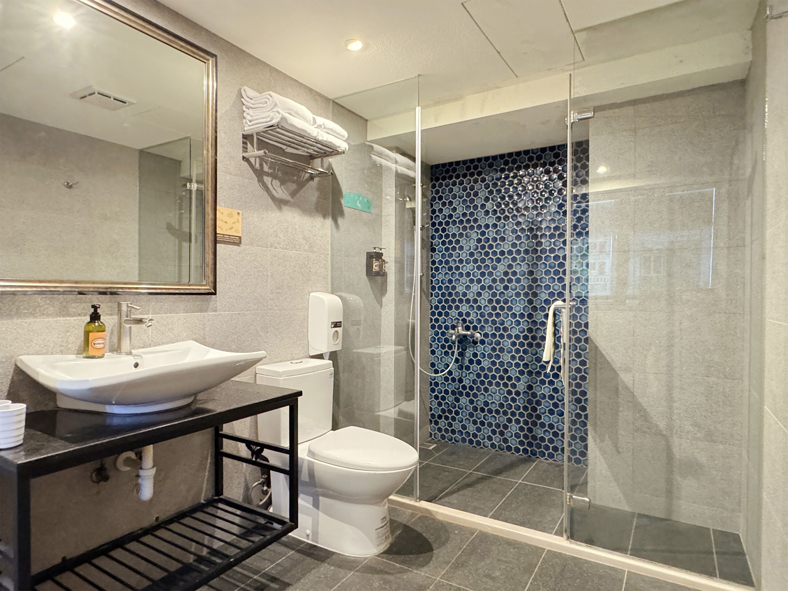 A modern bathroom with a large white sink, a toilet, and a glass-enclosed shower with a blue mosaic tile wall.