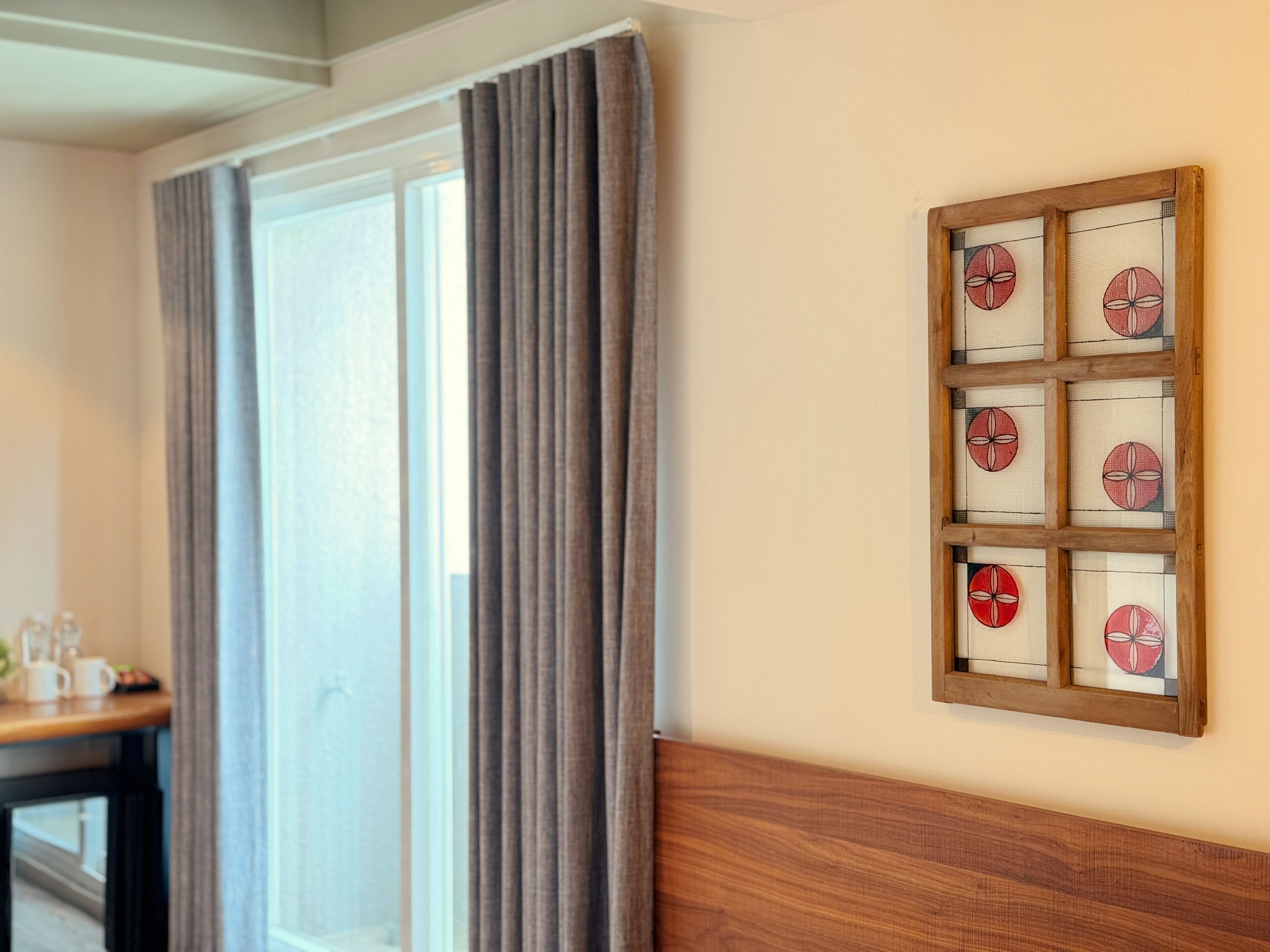 A room with a large window, a wooden headboard, and a wall-mounted decorative panel with circular patterns.
