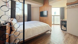Ein modernes Hotelzimmer mit einem großen Bett, Holzboden, einem an der Wand befestigten Fernseher und einem Fenster mit Blick auf die Stadt.