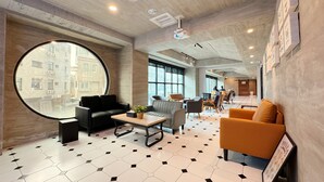 Eine moderne Hotellobby mit einem großen Rundfenster, einem Boden mit sechseckigem Muster und einer Sitzecke mit Sofas und einem Couchtisch.