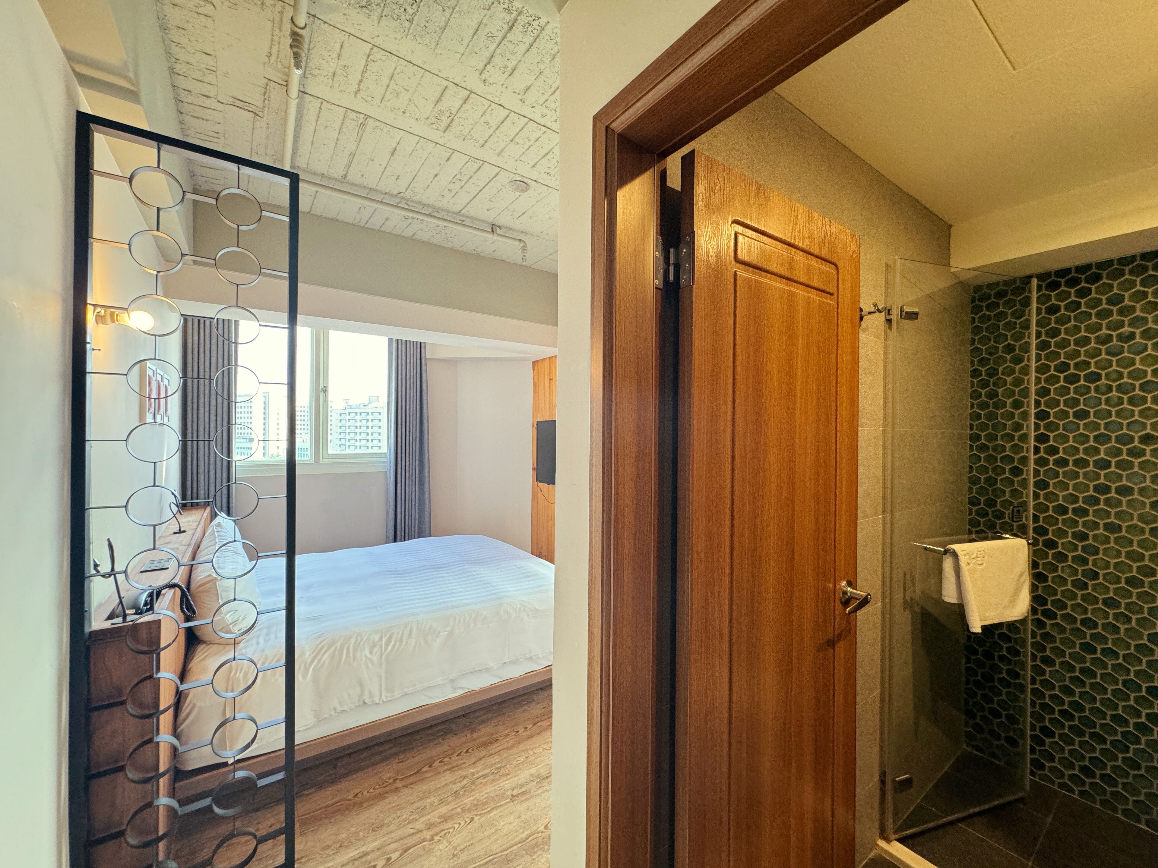 A hotel room with a bed, a wooden door, and a shower with a hexagonal tile wall.