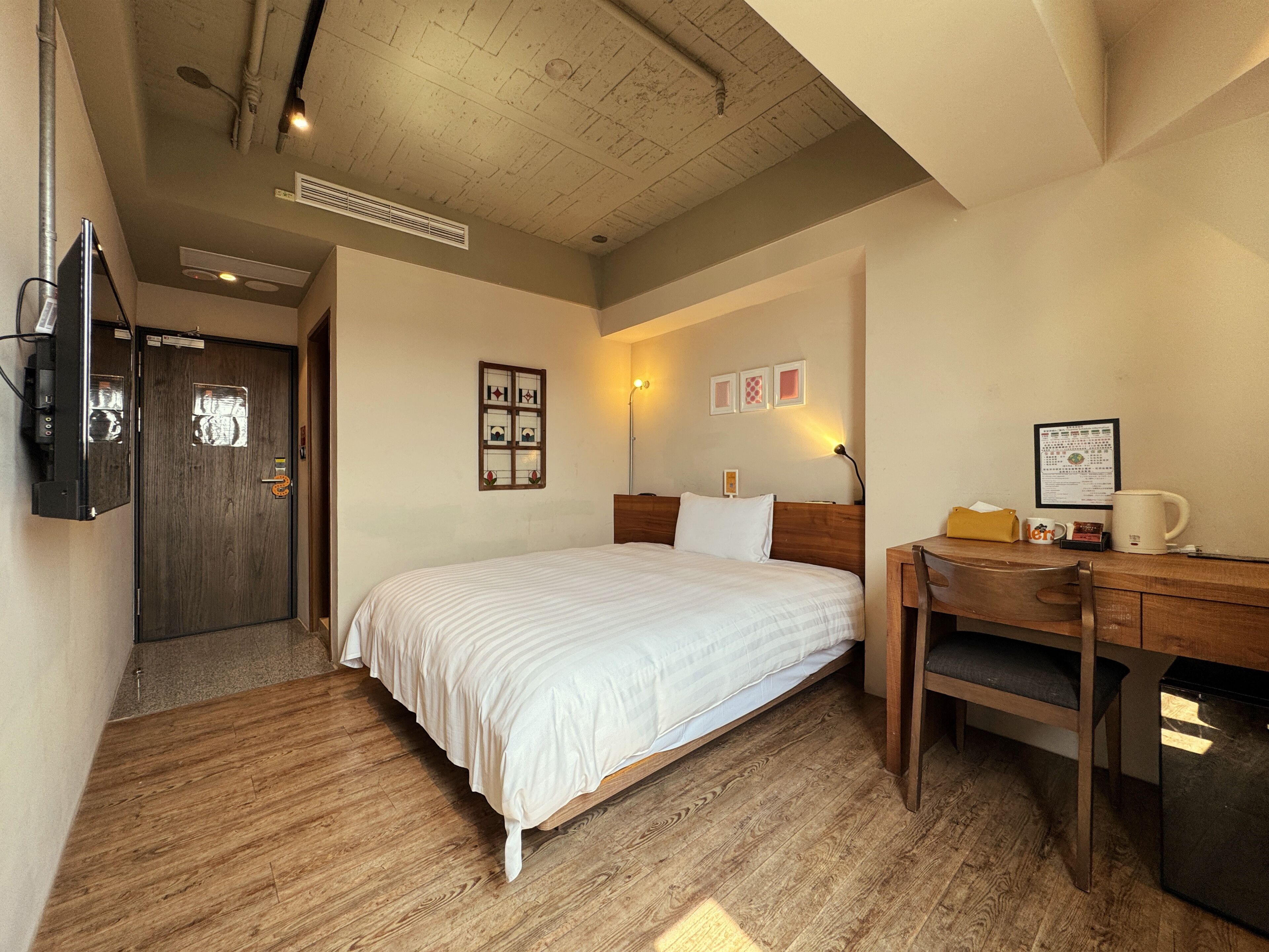 A hotel room with a bed, wooden desk, and a television mounted on the wall.