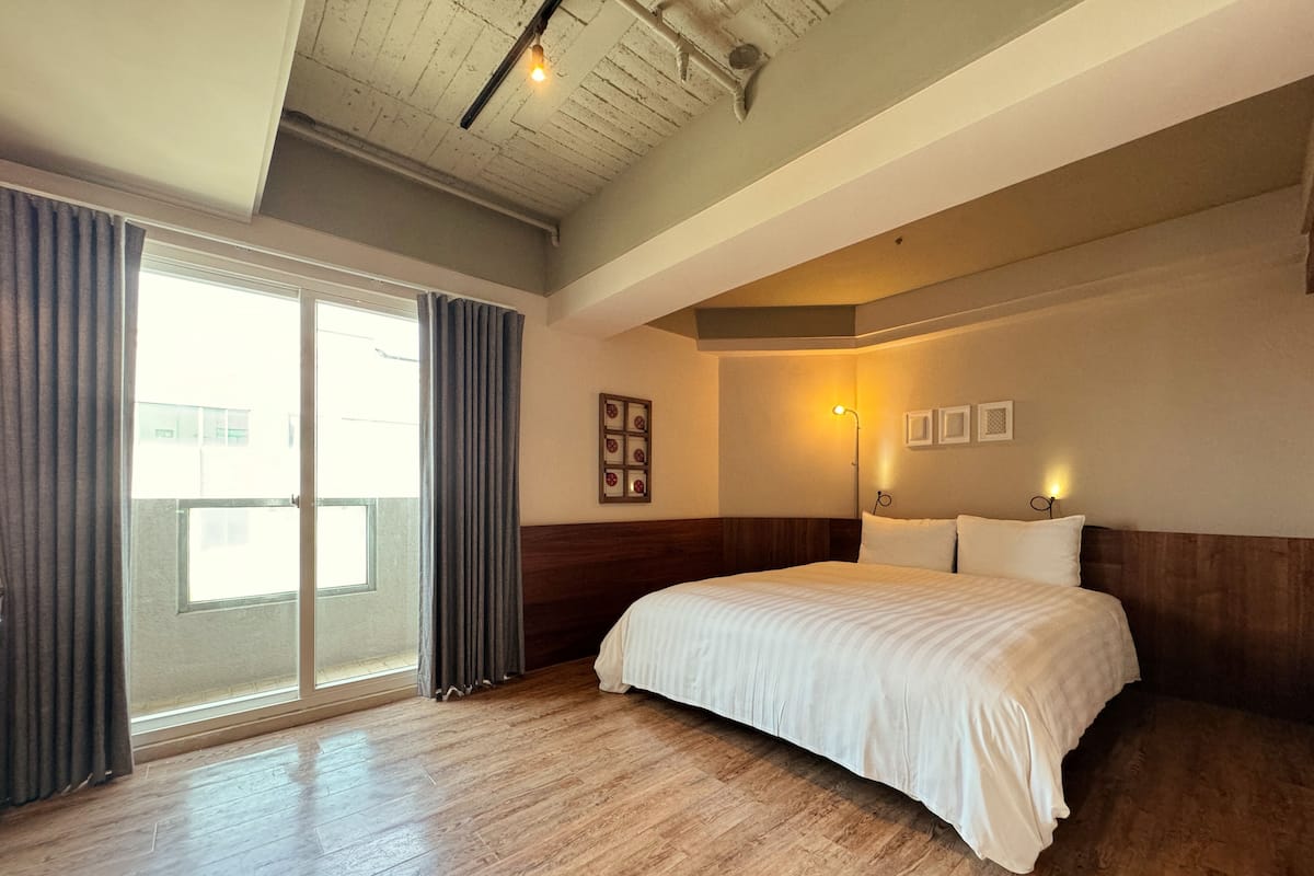 Ein Hotelzimmer mit einem großen Bett, Holzboden, einer Schiebeglastür und einer Decke mit sichtbaren Balken.