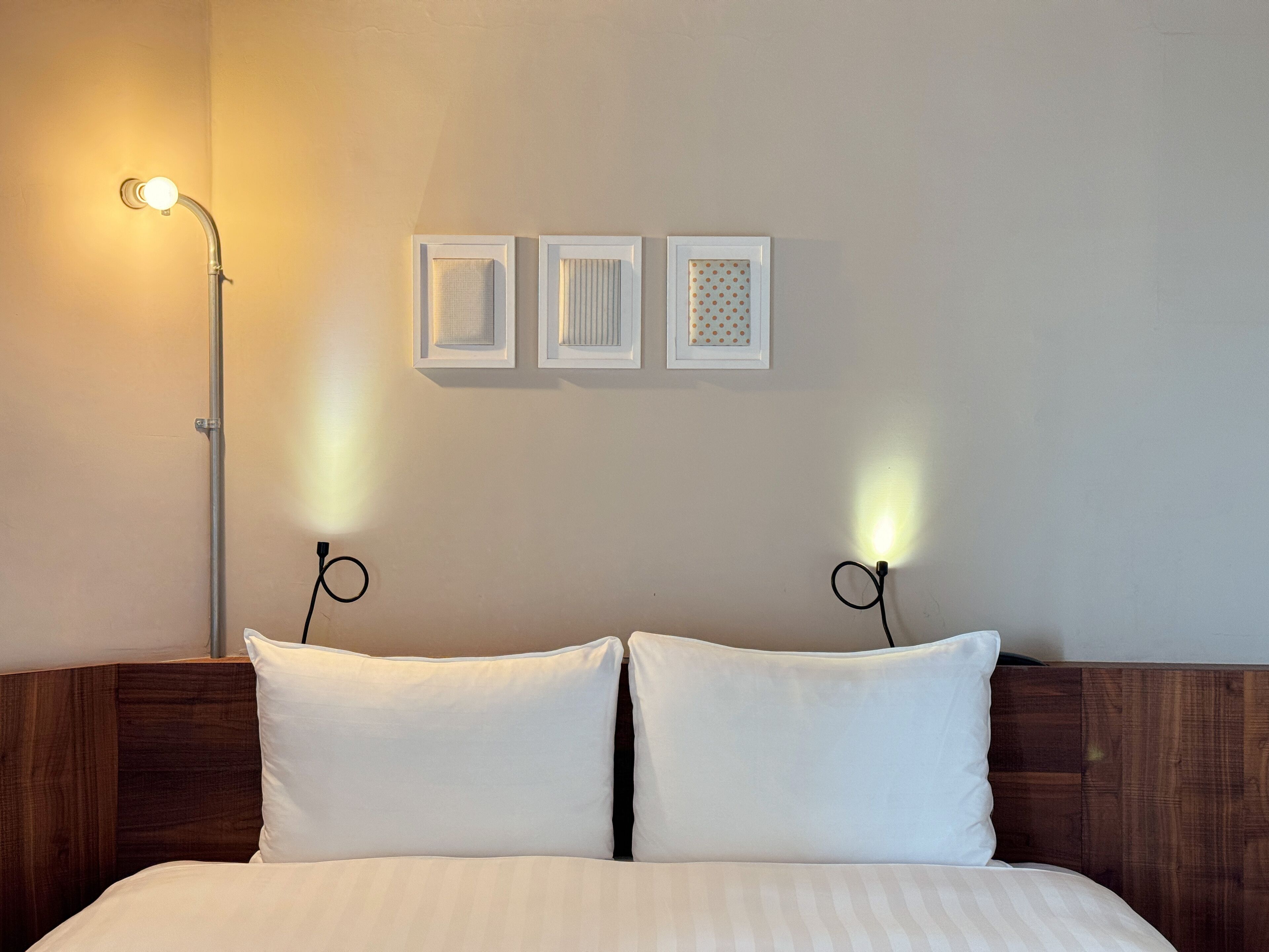 Una cama bien hecha con dos almohadas y un cabecero de madera. Encima de la cama, hay tres cuadros enmarcados en la pared.