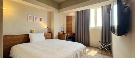 A hotel room with a large bed, a desk, a chair, a TV, and a window with curtains.
