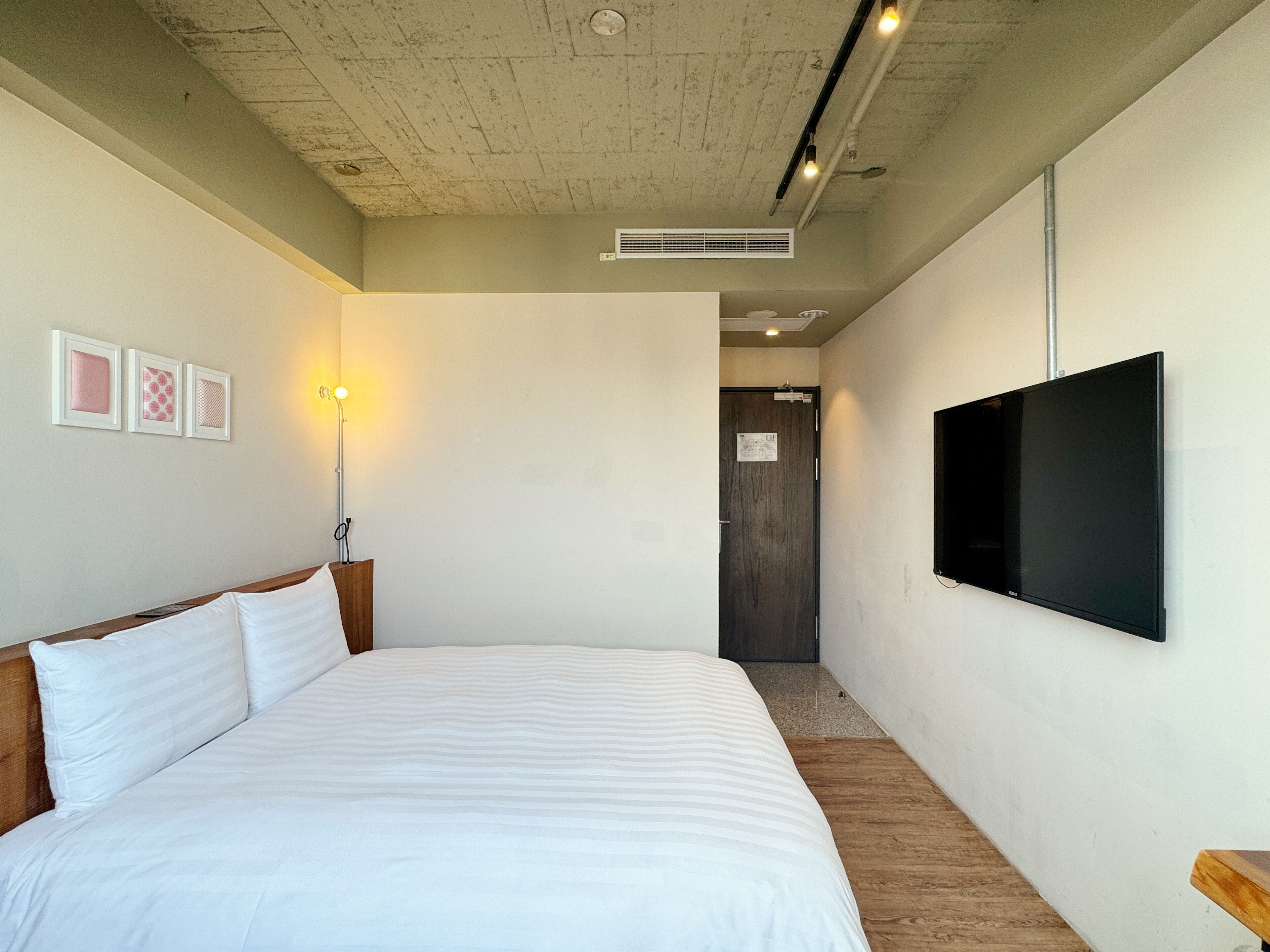 A hotel room with a large bed, a flat-screen TV mounted on the wall, a bedside lamp, and a small wooden side table.