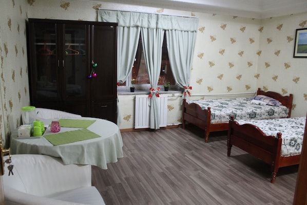 Un dormitorio con dos camas, un armario de madera, una mesa con mantel verde y una ventana con cortinas.