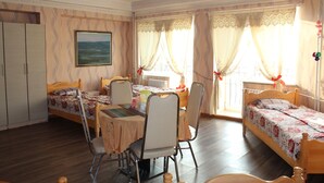 A room with two single beds, a dining table with chairs, a radiator, and a window with curtains. - Sara's Guest House (Ulaanbaatar)