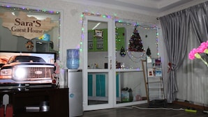 A room with a television, a water dispenser, a Christmas tree, and a sign reading "Sara's Guest House". - Sara's Guest House (Ulaanbaatar)