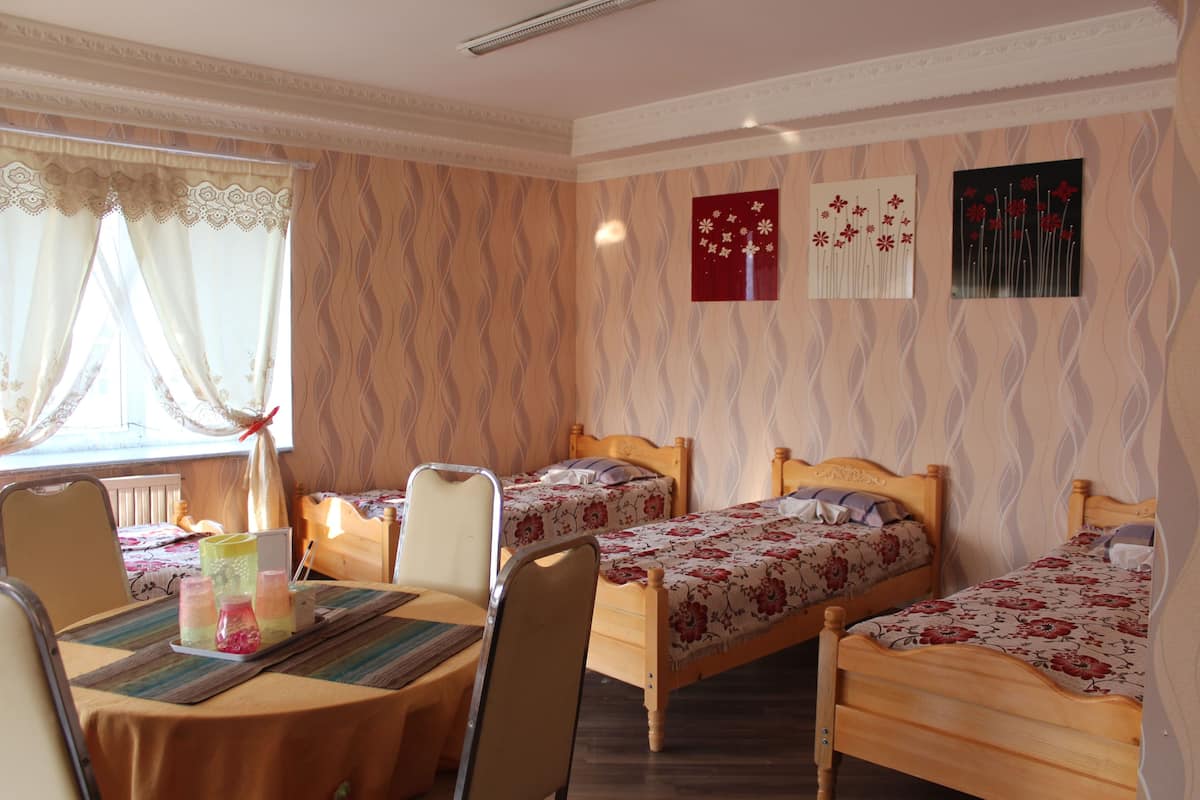 A hotel room with two wooden beds, a dining table with chairs, and a window with curtains.
