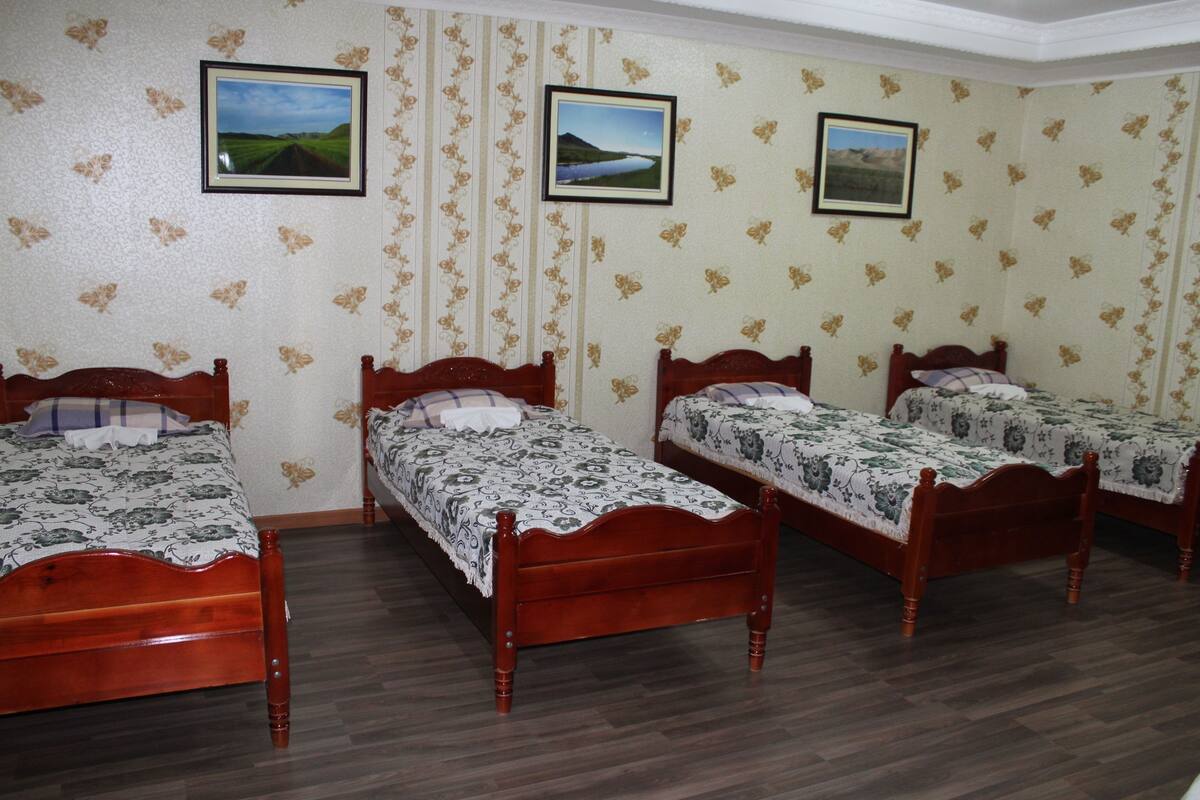 A room with four wooden beds, floral wallpaper, and three framed pictures on the wall.
