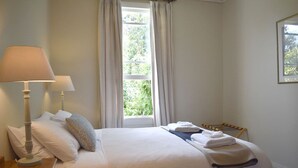 A neatly made bed with white linens, a bedside lamp, and a window with curtains.