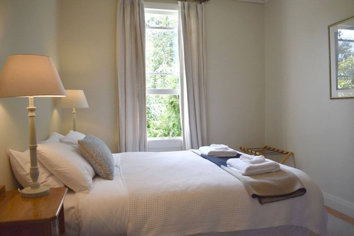A neatly made bed with white linens, a bedside lamp, and a window with curtains.