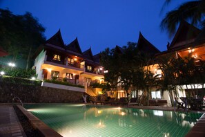 Un hotel con piscina, varios balcones y exuberante vegetación tropical.