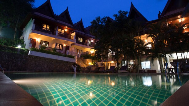 Un hotel con piscina, varios balcones y un entorno tropical.