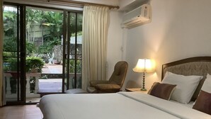 Habitación de hotel con cama, una silla, una lámpara y vistas a zonas verdes a través de una puerta corrediza.