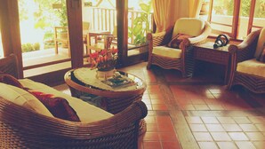 Una habitación luminosa con muebles de mimbre, suelo de baldosas y vistas al exterior.
