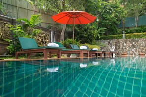 Un área de piscina con sillones de descanso y una sombrilla.
